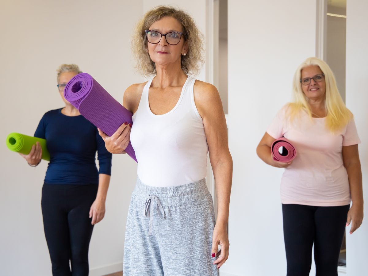 Three people holding exercise mats before a fitness class
