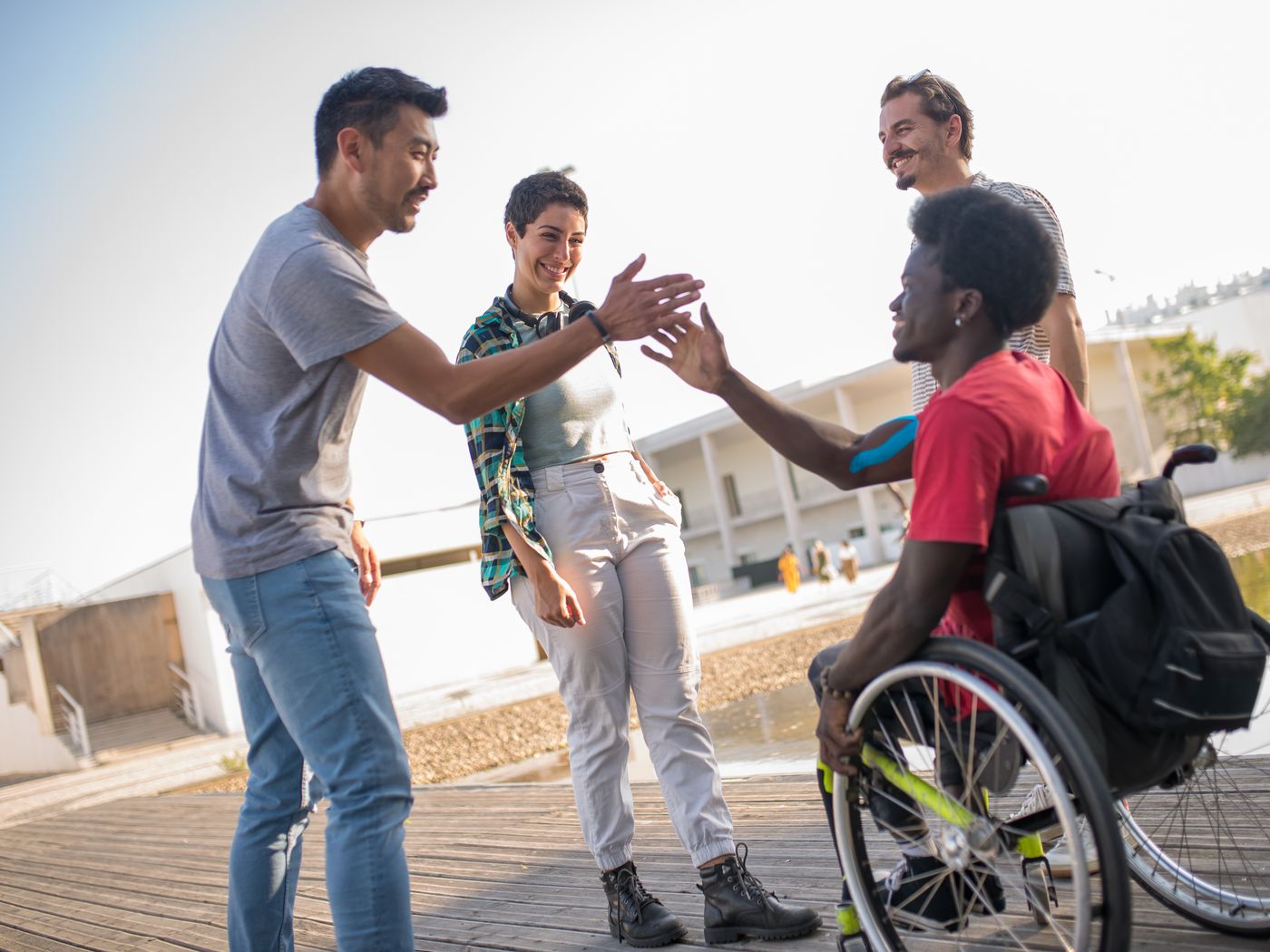 Friends greeting each other warmly outdoors, including a wheelchair user